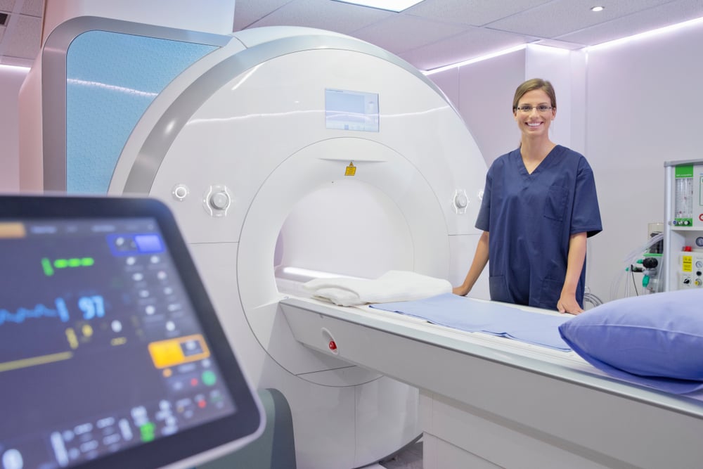 Mulher tecnóloga em Radiologia ao lado de máquina de ressonância magnética